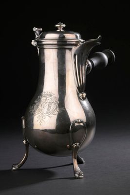 une cafetière ancienne en argent posée sur un socle, sur fond noir