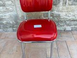 a red chair with a label on it sitting in front of a stone wall