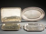 trois plateaux en argent et un plateau en argent muni de poignées, posés sur une table
