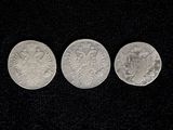 three silver coins sitting side by side on a black surface