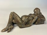 bronze statue of a woman laying on her stomach on a white surface