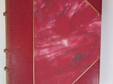 an old book with a red cover sitting on a white surface