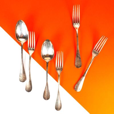 Plusieurs fourchettes et cuillères sont alignées sur un fond orange et blanc