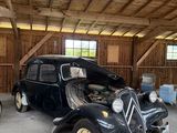 Plusieurs vieilles voitures sont garées dans un garage au plafond en bois.