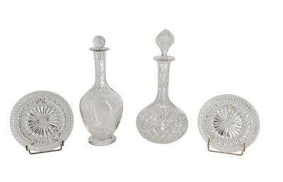 trois vases en verre et une assiette posés sur un support, le tout sur une surface blanche
