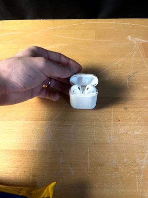 une personne tenant des AirPods d'Apple posés sur une table en bois