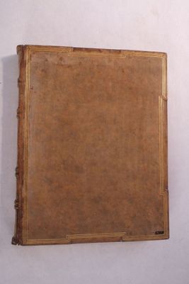 un vieux livre posé contre un mur blanc, avec une couverture marron