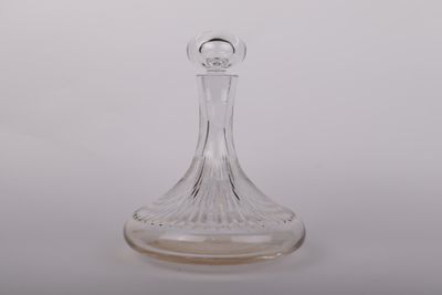 une carafe en verre transparent posée sur une surface blanche, avec un fond blanc