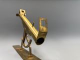 un petit pistolet en laiton posé sur un socle, sur une surface blanche