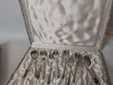 silverware in a silver case sitting on a table next to a cup and saucer