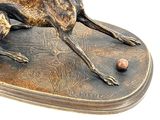 bronze sculpture of a dog laying down on a cushion with a ball