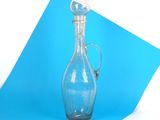une bouteille en verre bleue avec une poignée argentée, posée sur un morceau de papier bleu
