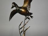 une photo d'une sculpture en bronze représentant un canard posée sur un socle en bois