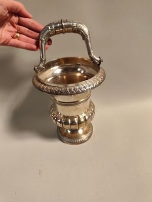 a person holding a silver vase with a handle