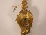 a gold clock hanging on the wall with a bird on it