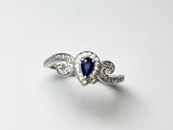 un gros plan d'une bague en forme de cœur sertie de diamants et de saphirs, posée sur une surface blanche