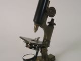 Un vieux microscope est posé sur un support, sur une surface blanche.