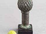 un petit vase en métal contenant une poire, posé sur un socle