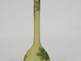 a green vase with leaves on it sitting on a white surface