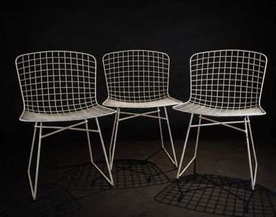 three white wire chairs sitting next to each other in a dark room