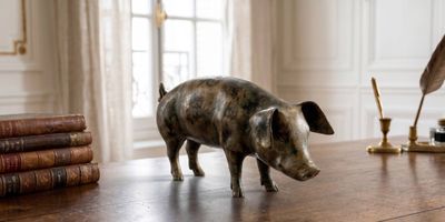 une statue représentant un cochon debout sur une table, à côté d'un stylo et d'un encrier