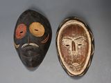 deux masques en bois posés sur une table, sur fond gris