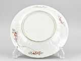 a white plate with red flowers on it sitting on a stand