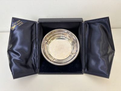 une assiette en argent vide dans une boîte noire posée sur une surface blanche