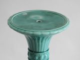 a green vase sitting on a table with a white wall in the background