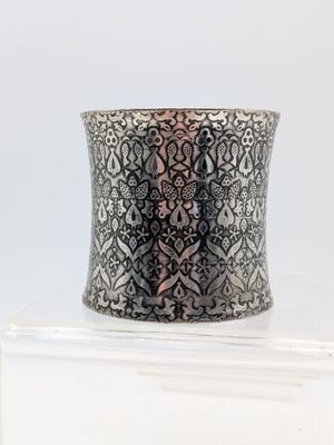 un gros plan d'un bracelet manchette en argent posé sur une surface blanche