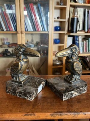 une paire d'oiseaux en bronze servant de serre-livres, posés sur une table en bois devant une bibliothèque