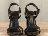 black leather high heeled sandals with gold accents on a wooden surface