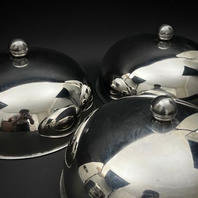 trois plats recouverts d'argent posés sur une table noire