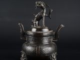 une vieille théière en bronze surmontée d'un chien