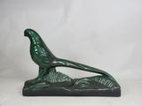 a green bird figurine sitting on top of a wooden base
