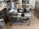 un chariot en acier inoxydable sur lequel sont posés des saladiers et des casseroles, dans une cuisine
