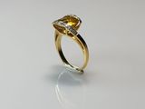 a close up of a yellow sapphire and diamond ring on a white surface