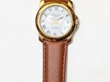 une montre en cuir marron avec un cadran blanc posée sur une surface blanche