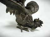 a silver figurine of a rooster on a white surface