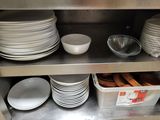 several plates and bowls are stacked on a metal shelf in a kitchen