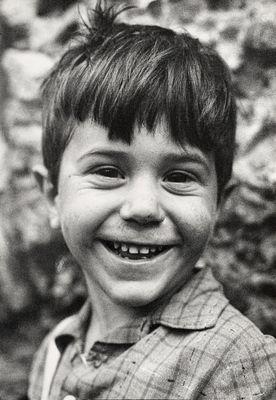 photographie en noir et blanc d'un jeune garçon souriant devant un mur de pierre