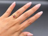 hand with pink manicured nails and a gold ring with a ruby stone