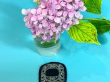 purple flowers in a vase with a black broocher next to it