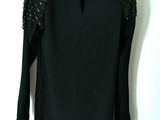 the top of a black top with sequins on it hanging on a hanger