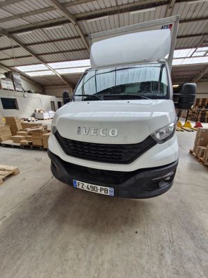 La camionnette blanche est garée dans un entrepôt où se trouvent des palettes et des cartons.
