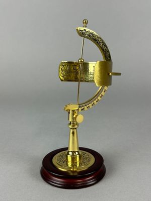 un cadran solaire ancien en laiton posé sur un socle en bois, avec un fond blanc