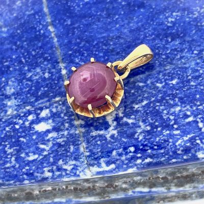 a close up of a pink stone pendant on a blue surface