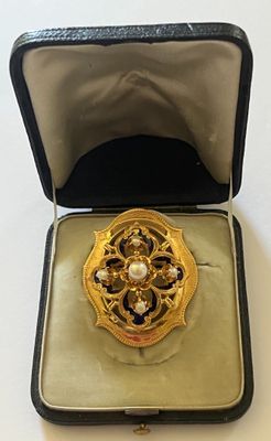 une broche en or dans un écrin noir posé sur une table blanche