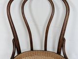 an antique wooden chair with wicker seat against a white wall
