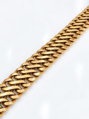 gros plan d'un bracelet en chaîne en or sur une surface blanche